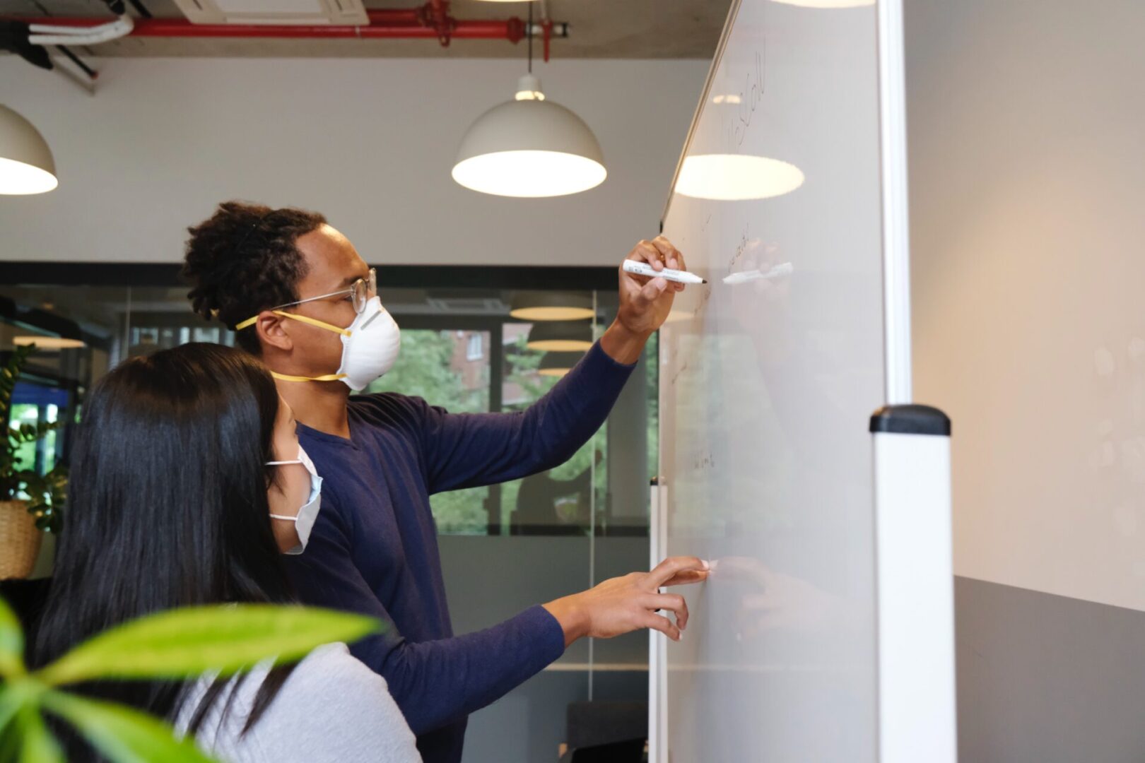 A woman wearing a mask and writing on a whiteboard.