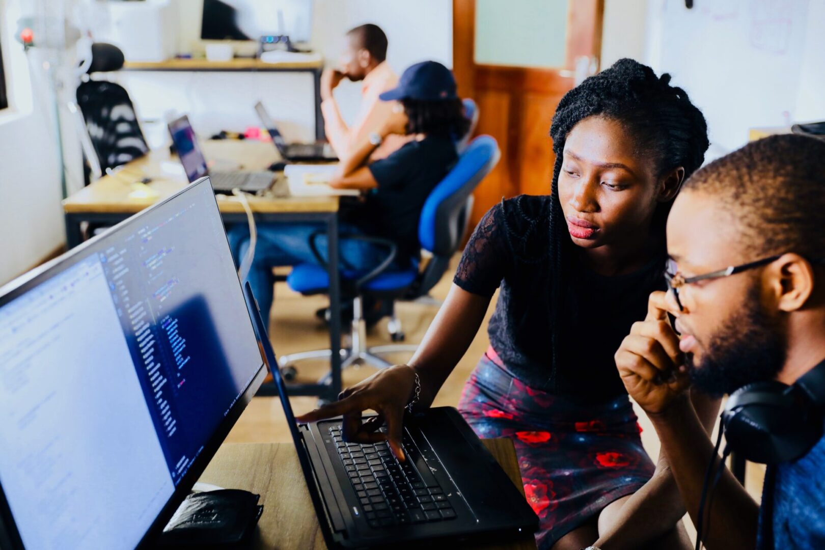 Two people are sitting at a desk with laptops.